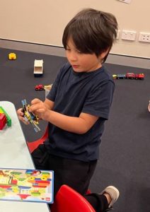 Child sits next to table and constructs a toy LEGO plane 