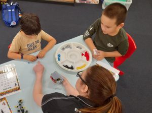 Two young lads play with LEGO on atble with Kristie Robbins overseeing the activity