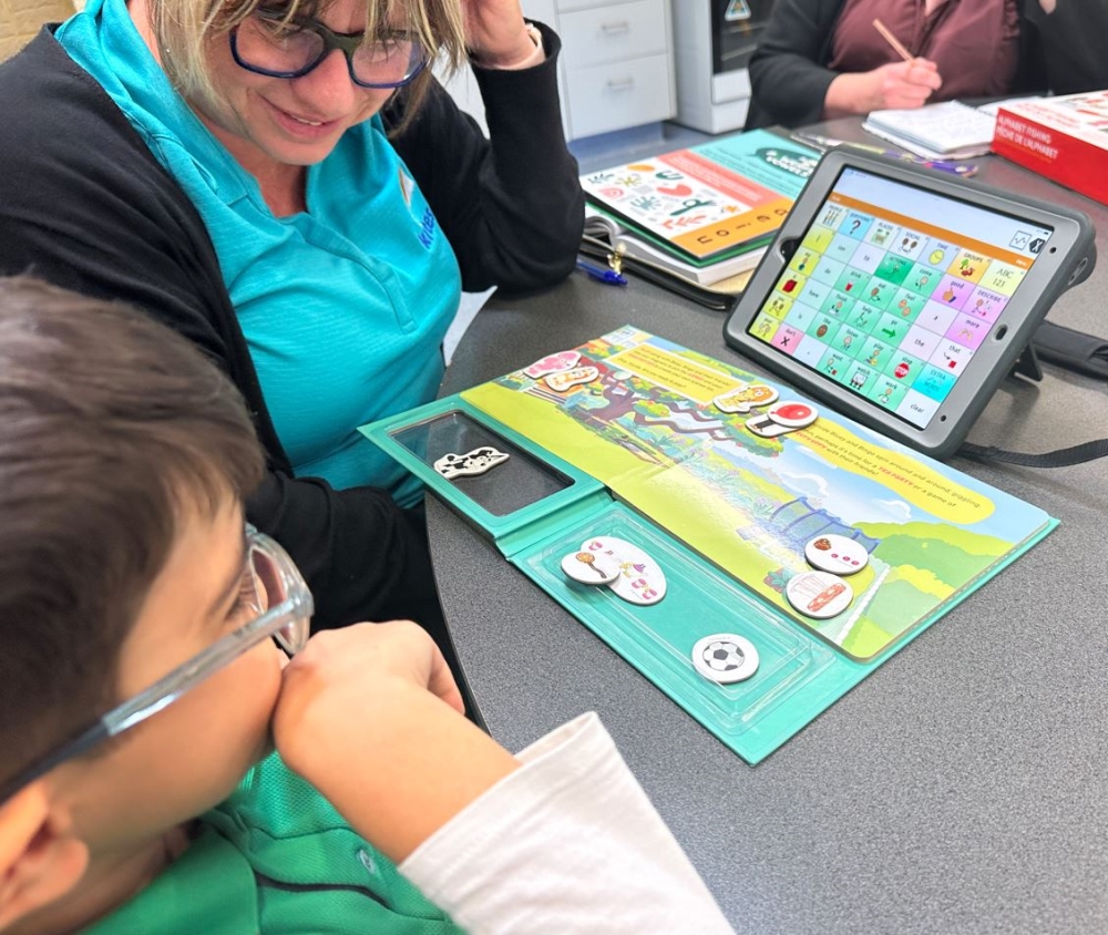 Image shows a speech pathologist looking at a child with the magnetic book and augmentative and alternative communication device in front of him 